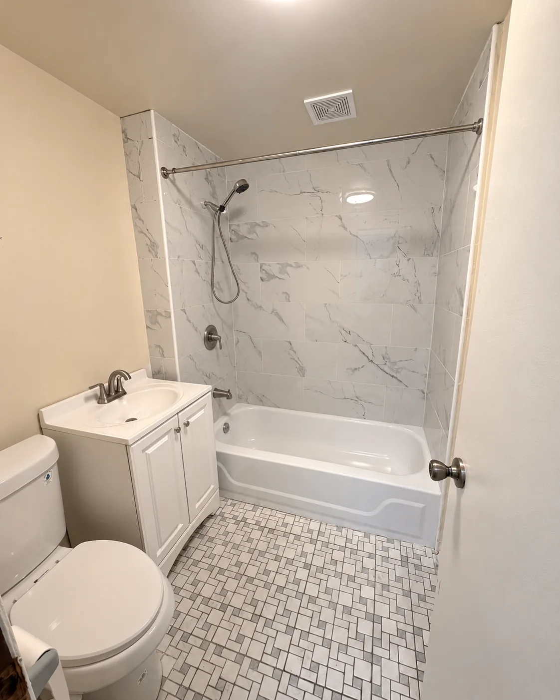 Completed bathroom with marble-look wall tile and clean white bathtub, with no shower curtain